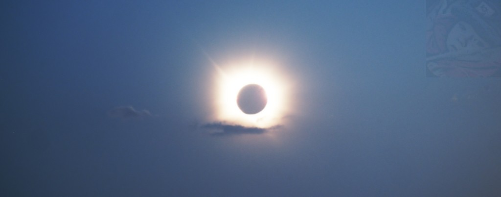 Bright yellow orona at totality time during the eclipse, with a fleeting cloud set as a hand under the floating dark moon.